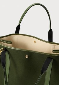Zelená látková taška na rameno s černými uchy, zlatými kovovými prvky a béžovým interiérem. Obsahuje zapínání na patent a otevřený úložný prostor.