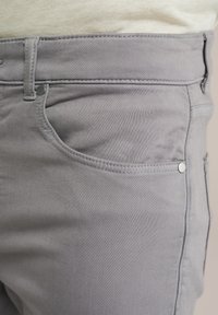 Gray cotton blend pants with front pockets, visible stitching, and silver hardware accents. The fabric is smooth and slightly stretchy.