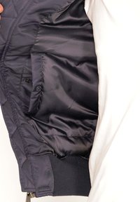 Schwarze gesteppte Jacke innen, ausgestattet mit einem glatten, satinähnlichen Stoff, vorn mit Knopfverschluss und gerippten Bündchen.