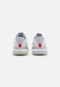 Des chaussures de sport blanches et grises présentent une tige en maille texturée, un col de talon rembourré et un accent rouge proéminent sur l'étiquette du talon.