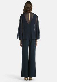 Conjunto de dos piezas en azul marino que incluye una blusa con capa fluida y abertura en la espalda, junto con pantalones de pierna ancha en una tela suave.
