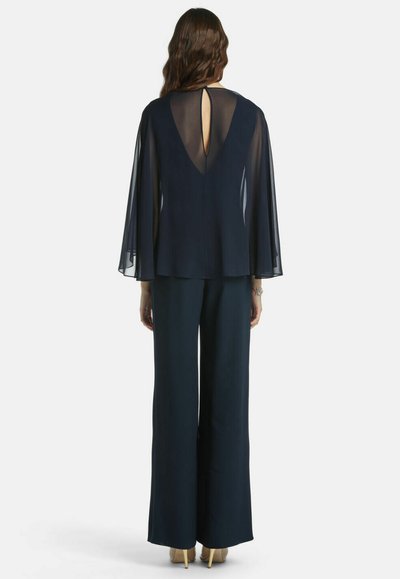 Marineblaues zweiteiliges Outfit mit einem fließenden Cape-Oberteil mit Schlüsselloch-Detail am Rücken und weit geschnittenen Hosen aus einem glatten Stoff.