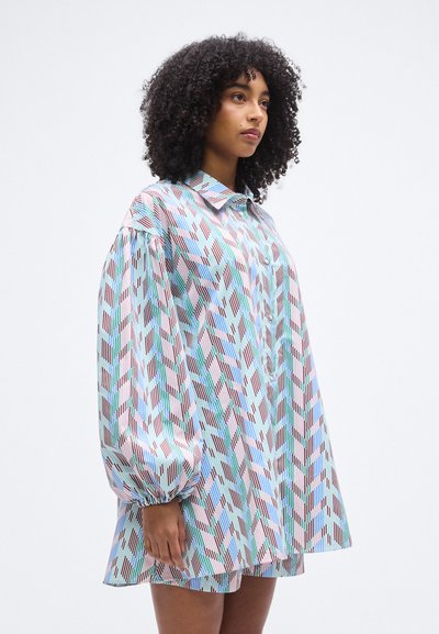 Ένα πολύχρωμο υπερμέγεθες πουκάμισο με γεωμετρικό μοτίβο σε ροζ, μπλε και πράσινο. Διαθέτει μυτερό γιακά και φουσκωτά μανίκια. Κατασκευασμένο από λείο ύφασμα.