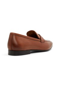 Mocasines de piel marrón con punta redondeada, suela plana negra y costuras minimalistas. Presentan un sutil acento cerca del empeine.