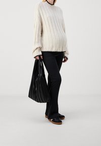 Överstor krämfärgad tröja med ribbad textur och svarta detaljer, kombinerad med svarta byxor och en veckad svart tote-väska, tillsammans med rundade skor.