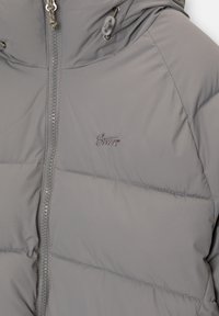 Siva podložena jakna z visokim ovratnikom, osrednjim zadrgo in nastavljivimi vrvicami. Ima subtilno vezenje logotipa in gladko teksturo.
