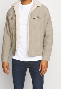 Beige kordflorjacka med en fluffig vit foder, med knappstängning fram, två bröstfickor och en något kortare passform.