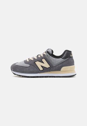 Szaro-beżowy sneaker New Balance z panelami z zamszu i siateczki, beżowymi sznurówkami oraz czarną gumową podeszwą, widoczny z boku na białym tle.