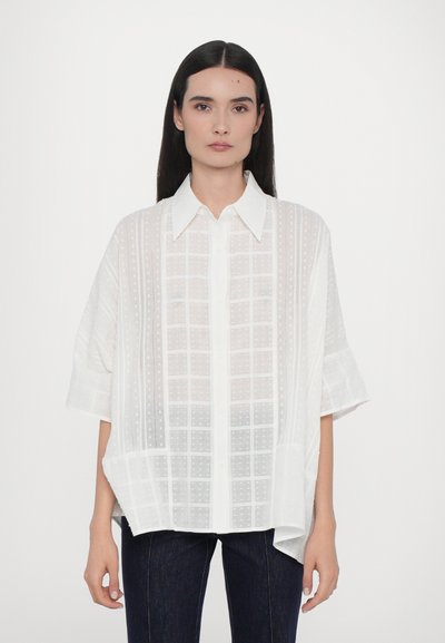 Chemise blanche surdimensionnée à boutons avec des manches courtes. Présente un motif en grille texturé et un col pointu. Le tissu semble léger et transparent.