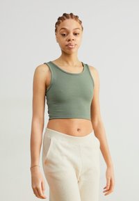 Green sleeveless crop top with a ribbed texture, paired with light cream sweatpants. The top features a rounded neckline and fitted design.