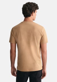 Camiseta de manga corta, de cuello redondo, en un color marrón claro sólido, hecha de un tejido suave con una textura lisa, mostrando un diseño liso en la parte posterior.