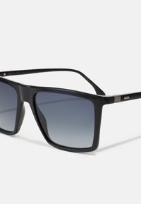 Black square-shaped sunglasses with gradient gray lenses, made of plastic. Features a sleek design and subtle branding on the temples.