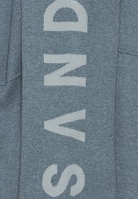 Tessuto blu heather con grandi lettere bianche "SAND" sul davanti. Il materiale sembra morbido con una finitura texturizzata.