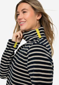 Haut en polaire rayé bleu marine et crème avec un col montant et une accentuation jaune au niveau du col et des poignets. Texture douce, coupe décontractée.