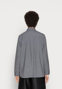 Grå skjorta med krage, slät yta, långa ärmar, knäppning vid handlederna och rak design i ryggen. Inga synliga mönster eller dekorationer.