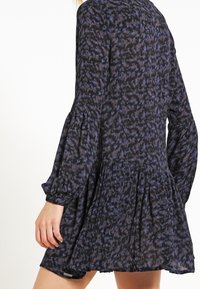 Abito nero con un motivo astratto blu, maniche puff lunghe, corpino aderente e gonna svasata. Tessuto morbido con una sottile texture.