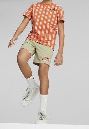 T-shirt à manches courtes rayé orange avec un logo noir, associé à un short beige avec un patch logo, des chaussettes blanches et des baskets claires.