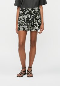 Black mini skirt with white abstract patterns, featuring a side tie detail. Worn with black strappy sandals. Smooth fabric texture.