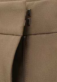 Jupe en tissu marron avec une fermeture éclair invisibile et deux accents en métal à la taille, mettant en avant un design épuré et ajusté.