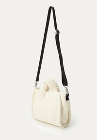 Bolso de shearling blanco y esponjoso con forma rectangular, correa ajustable negra y dobles asas superiores. Los acentos incluyen herrajes de plata.