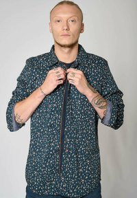 Navy overhemd met bloemenpatroon en lange mouwen. Kenmerkend zijn de contrasterende oranje accenten en de denim stof bij de manchetten.