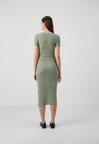 Vihreä neulebodycon-mekko, jossa on lyhyet hihat, raidoitettu pinta, polvipituinen, pyöreä pääntie ja hienoinen venyvyys. Mustat kengät.