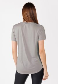 Camiseta gris de manga corta con dobladillo redondeado, textura suave y diseño sencillo. La vista posterior muestra detalles de la costura del hombro.