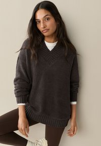 Tumehall suur sukasärk pehmest, tekstuuriga kangast, V-kaelusega ja soonikkoes varrukaotstega. Kanditud valge särgi peale ja kombineeritud pruunide retuusidega.