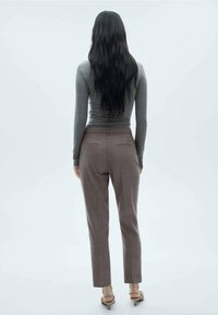 Haut gris ajusté à manches longues associé à un pantalon marron sur mesure, doté de poches arrière et d'un design de jambe fuselée. Le modèle est de dos.