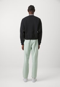 Sweatshirt preto com um design encurtado, combinado com calças de moletom verde claro, ambas feitas de um tecido macio. Ténis brancos completam o look.