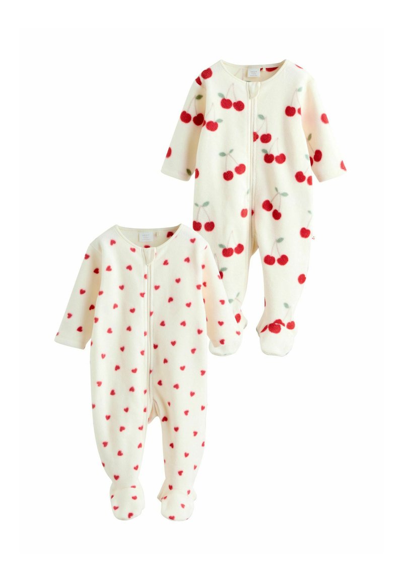 Kaksi lasten pyjamaa, joissa on kermaisen vaalea tausta. Toisessa on pieniä punaisia sydämiä, kun taas toisessa on punaisia kirsikoita vihreillä lehdillä. Molemmissa on vetoketju.