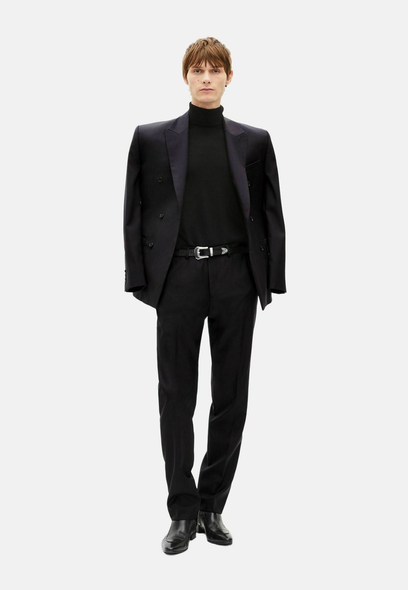 Black tailored suit featuring a double-breasted jacket, fitted turtleneck, and slim trousers, complemented by a belt and shiny black shoes.