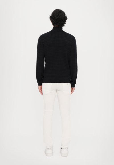 Pulover negru, tricotat cu textură, cu guler înalt, combinat cu pantaloni albi ajustați și adidași albi, care oferă o vedere din spate curată și minimalistă.