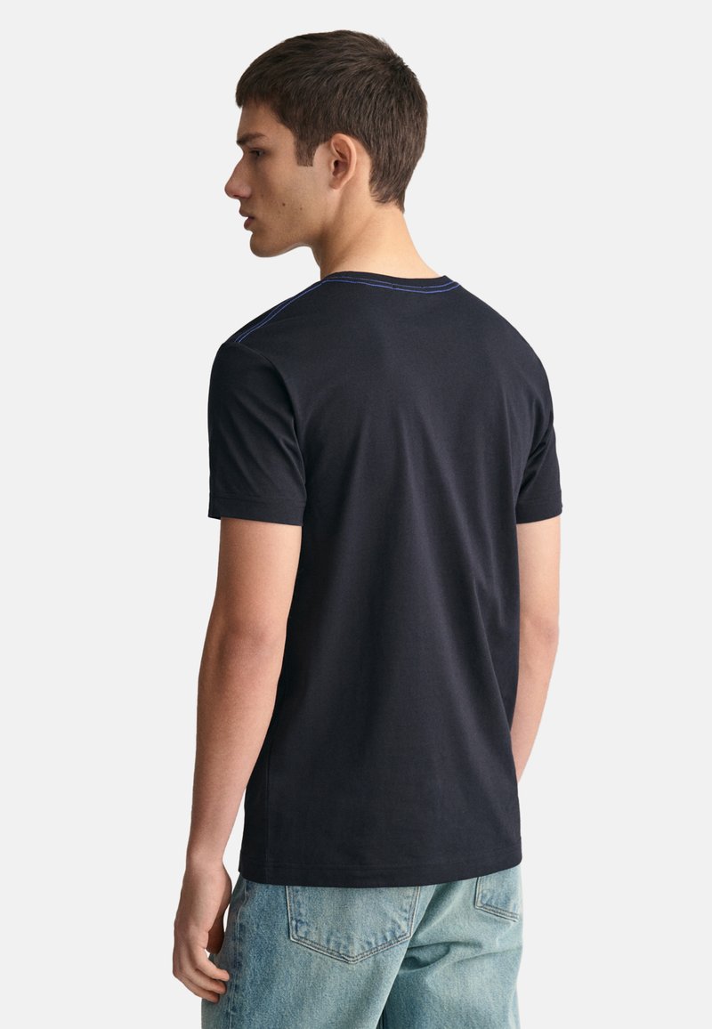 Camiseta negra de manga corta con cuello redondo, que presenta detalles de costura azul en el cuello y la parte posterior, fabricada con una tela suave.