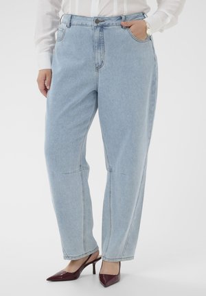 Person wearing light blue loose-fit jeans, white blouse, silver watch, and burgundy pointed-toe slingback heels, standing against a plain background.