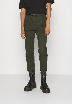 Olivgrüne Cargo-Hosen mit elastischem Bund und Kordelzug, mit tapered Knöchelbündchen, kombiniert mit schwarzen Schnürstiefeln.