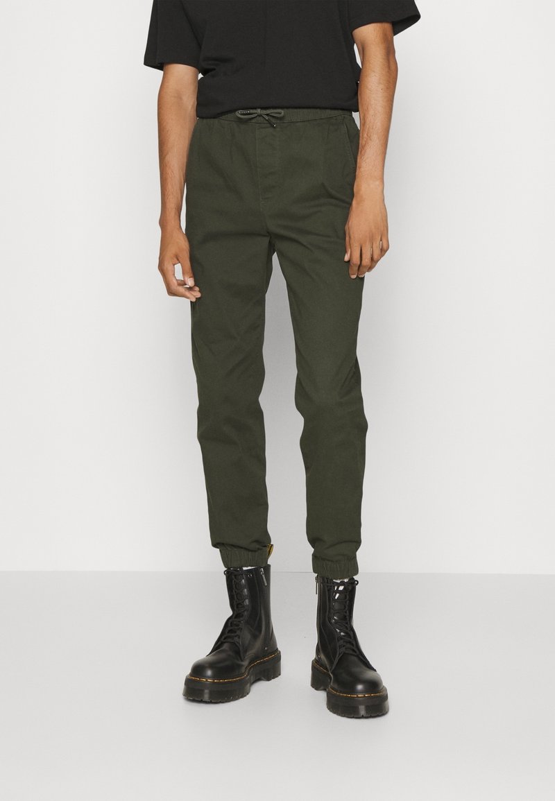 Olijfgroene cargobroek met een elastische tailleband en trekkoord, taps toelopende enkelboorden, gecombineerd met zwarte veterschoenen.