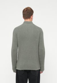 Pelēks ribots adīts džemperis ar augstu apkakli, garām raglana piedurknēm un teksturētu rakstu. Mīksts materiāls ar brīvu piegriezumu.