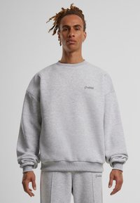 Szürke, lazán illeszkedő crewneck pulóver. Puha anyagból készült, bordás mandzsettákkal és egy kis hímzett logóval a mellkason.