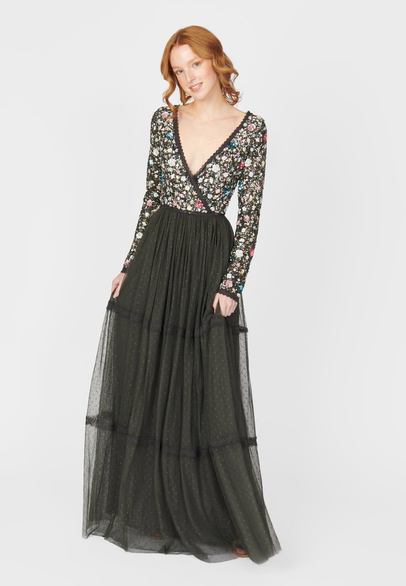 Vestido largo de un verde oscuro, con un corsé de manga larga con estampado floral. Presenta un escote en V y una falda en capas, transparente, con textura de puntos y acentos de encaje.