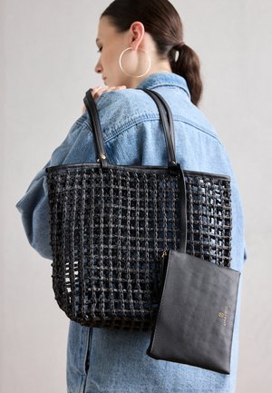 Zwarte gevlochten totebag met leren accenten, voorzien van twee stevige handvatten en een afneembare zwarte tas. De tas heeft een rechthoekige vorm en open vlechtwerk.