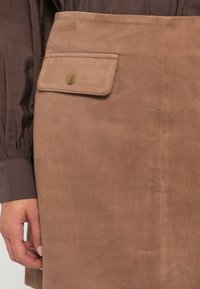 Suède rok in lichtbruin met een zijzak en een messing drukknoopsluiting. Soepele textuur met een minimalistisch ontwerp.