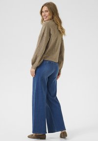 Pull en tricot marron clair avec un motif texturé, assorti à un jean en denim bleu à jambes larges et des mocassins marron décontractés.