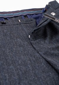 Dunkelblaue Hose aus strukturiertem Stoff mit Reißverschluss und Knopfverschluss sowie gestreiftem Detail am inneren Bund.