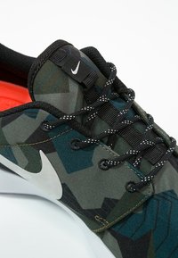 Tenisky Nike mají vícebarevný geometrický vzor v odstínech zelené a modré, černé tkaničky a bílý logo Swoosh po straně.