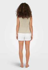Lichtbeige mouwloze gebreide top gecombineerd met witte shorts met opgerolde zomen. De outfit heeft een ontspannen pasvorm die geschikt is voor warm weer.
