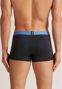 Svarta boxerkalsonger med en blå elastisk midjeband, som har en slät yta och en figurnära design, visade från baksidan.
