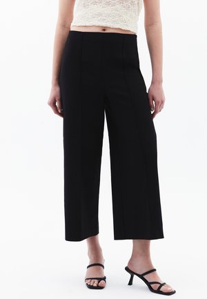 Zwarte wijde pijpen broek met een soepele textuur, voorzien van verticale stiksels en een hoge taille. Gecombineerd met open teen zwarte hakken.