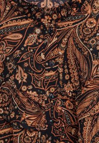 Blouse à motif cachemire marron et orange sur fond noir, avec un col volanté et quatre boutons noirs sur le devant.
