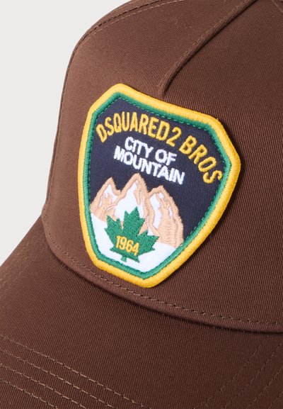 Casquette marron avec un écusson jaune, vert et bleu marine montrant des montagnes, une feuille d'érable verte et le texte "DSQUARED2 BROS CITY OF MOUNTAIN 1964."